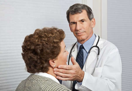 Doctor examining mature female patient for flu symptoms in officeの写真素材