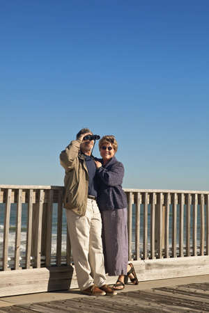 Happy mature, senior couple on a wooden seaside pier with the ocean in the background.の写真素材