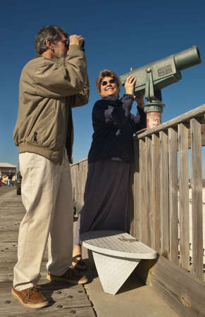 Happy smiling retired couple skywatching and birdwatching on a seaside fishing pier.の写真素材