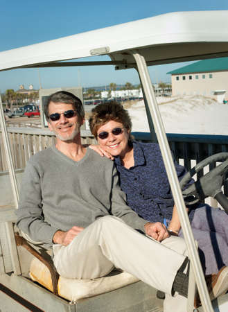 Happy retired couple having fun in an old golf cart at the beach.の写真素材