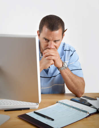 Young man looking tired, frustrated and worried as he sits at his desk with computer, checkbook and calculator.の写真素材