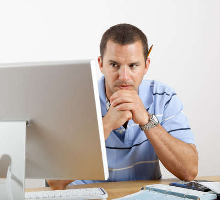 Young man at desk with computer, checkbook and calculator, worrying about paying the bills.の写真素材
