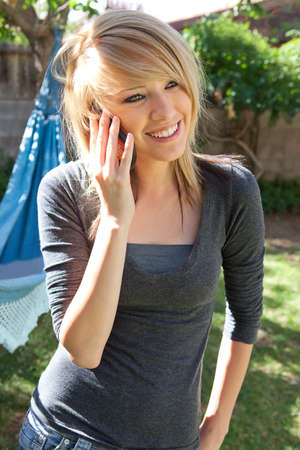 Pretty blond teenage girl talking on cell phone (mobile phone) outdoors on a sunny day.の写真素材
