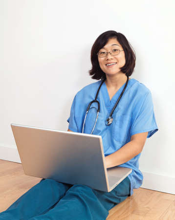Smiing woman nurse or doctor, seated on floor with laptop computerの写真素材