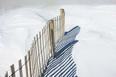 Sand fence and shadows on snowy white dunes at the beach.の写真素材