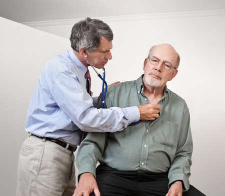 Male doctor listening to older man's heart with stethoscopeの写真素材