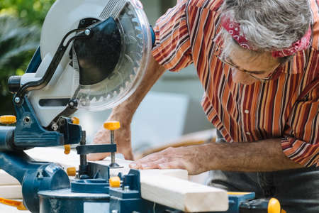 Closeup of mature man sawing lumber with sliding compound miter saw outdoors.
の写真素材