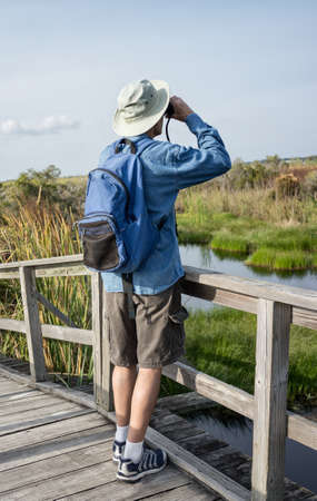 Man Birdwatching in Florida Wetlands on Weathered Wooden Foot Bridgeの写真素材