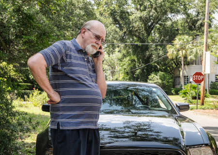 Angry elderly man on cell phone calls for roadside assistance for car malfunction or breakdown...