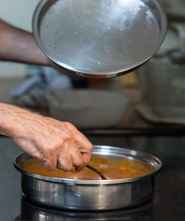 Short depth of field shot of man's hand stirring a pan of sauce on stove top