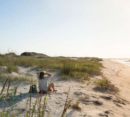 Seated woman in pristine sand dunes at Florida Gulf Coast beach looks out to sea as the sun rises.の写真素材