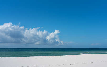 Uncluttered colorful summer beach background with puffy clouds, blue sky, turquoise water and white sandy beachの写真素材