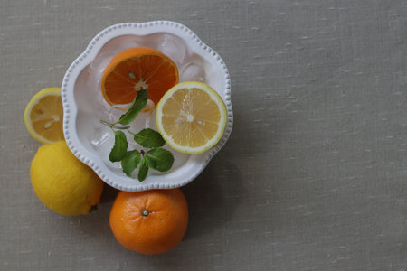 Slices of lemon, orange and mint in a white bowl on a gray background.
