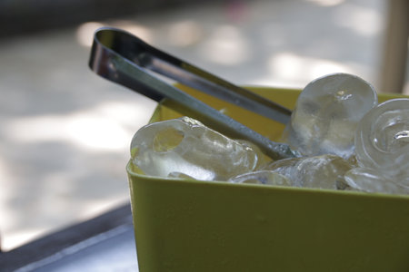 Ice cubes in a green plastic container with stainless steel tongs.