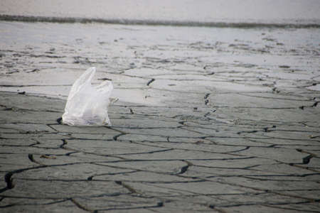 Pollution on the beach, plastic bag on the cracked sand, Environmental Crisis