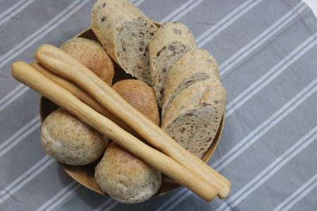 Bread and breadsticks in a wooden bowl on a gray background.