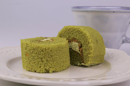 Green tea roll cake on white plate with cup of coffee in background