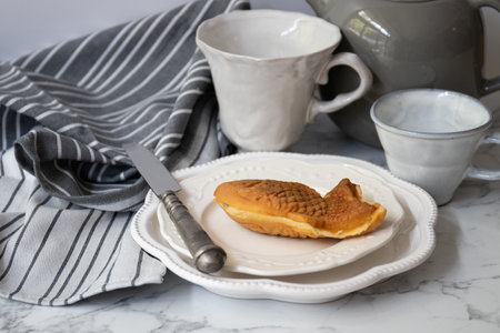 A piece of Japanese Dessert, Taiyaki,  on a plate with a knife and a cup of coffee