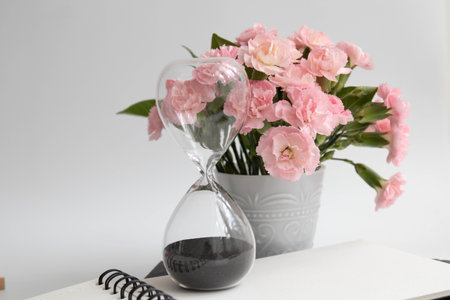 Bouquet of pink carnation flowers in a vase with hourglass
