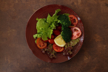 Healthy Dish , Green Salad from organics vegetable, Fresh Lettuce, Red Tomatoes, Bell Pepper, Lemon , Red Plate on Rustic Backgroundの写真素材