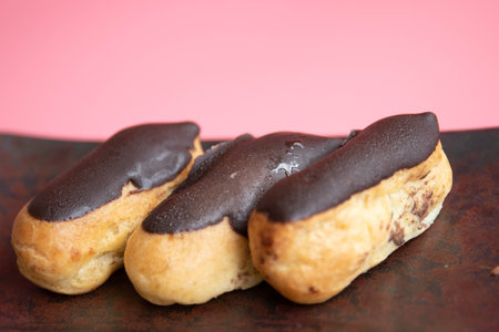 Chocolate eclairs on a metal plate on a pink background