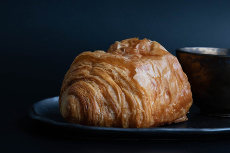 Croissant and cup of coffee on black background, close up