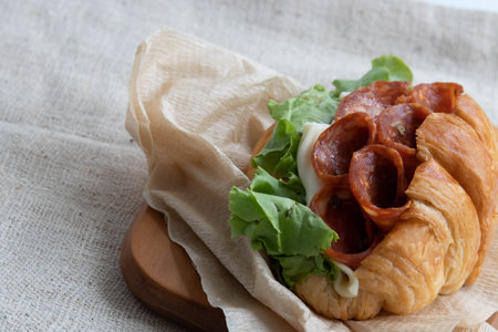 Croissant sandwich with salami, cheese and lettuce on wooden boardの写真素材