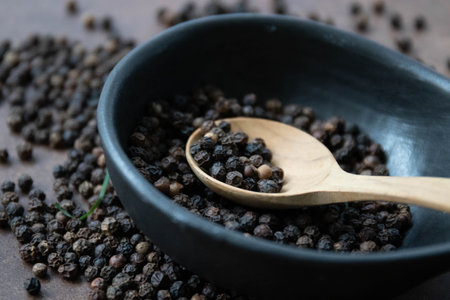 Black pepper in a bowl and wooden spoon on wooden table background.