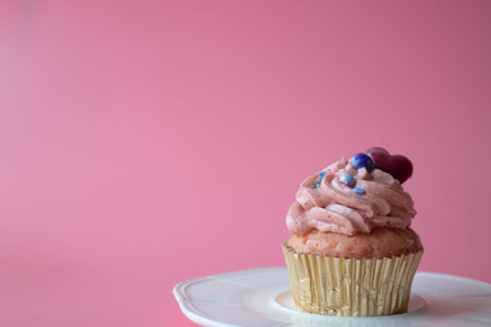 Vanilla Cup Cake topped with Pink Whip Cream and Red Heart on Pink Background