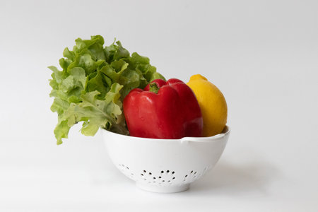 Vegetables in a white colander on a white background.