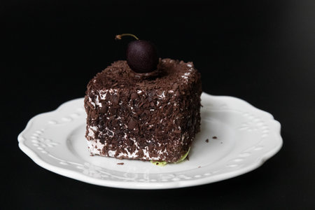 Chocolate cake with cherry on a white plate on a black backgroundの写真素材