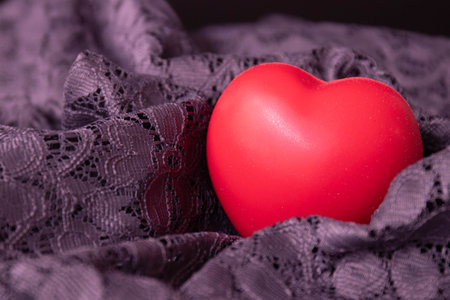 Red heart on a black lace background. Selective focus. Toned.