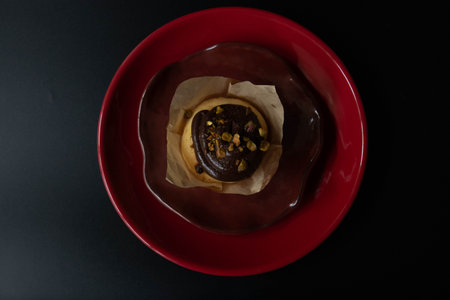 Chocolate cake with nuts on a red plate on a black background