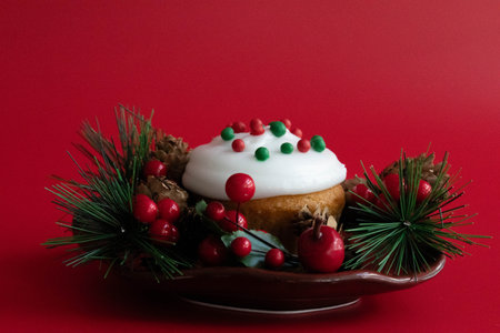 Christmas cupcake with white frosting on a red backgroundrated with pine cones and berriesの写真素材