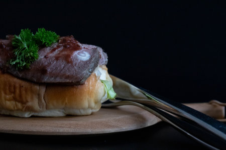 Beef burger on wooden plate with fork and knife on black background