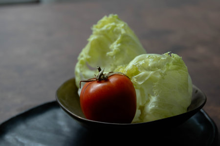 Lettuce and tomato in black bowl on wooden table background.の写真素材