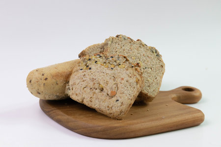 Golden-brown rolls, flecked with dark seeds and oat flakes in a white bowl, white background