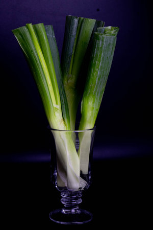 Fresh spring onions in a glass vase on a black background.の写真素材