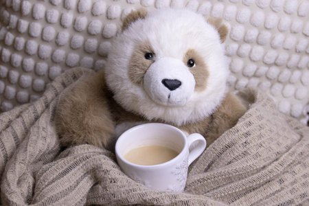 Little Brown Panda plush doll is having coffee under a warm blanket