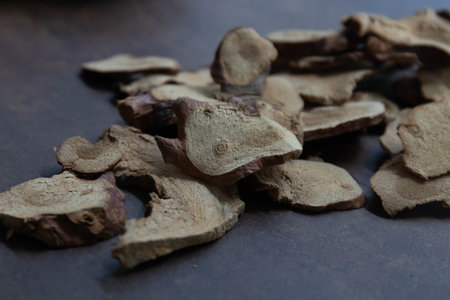 A black bowl filled with Galangal slices, with additional pieces scattered on a dark textured...