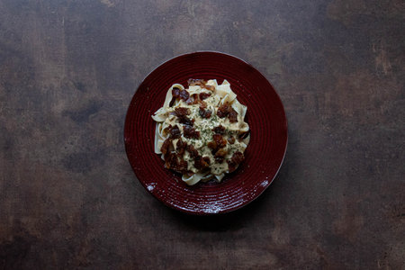 Fettuccine Alfredo , A comforting plate of fettuccine pasta coated in a rich, creamy sauce and topped with crispy bacon piecesの写真素材