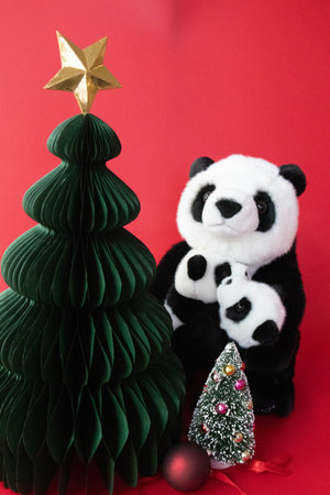 A cozy holiday scene featuring a plush panda mother cuddling her baby beside two Christmas treesの写真素材