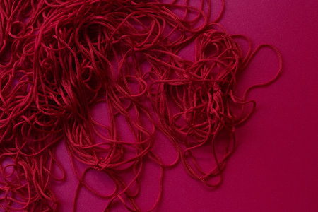 A heap of intertwined red cords spread across a deep magenta surface. The loops and twists form an intricate, abstract pattern that contrasts the smooth backgroundの写真素材