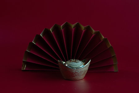 A refined still life featuring an ornate silver Chinese ingot placed before a fully opened folding fan.の写真素材