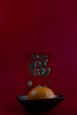A minimalist still life featuring an orange set against a deep red background, symbolizing wealth, luck, and abundance. Behind it stands the bold black Chinese character âç¦â (Fu), meaning blessing or good fortune.の写真素材