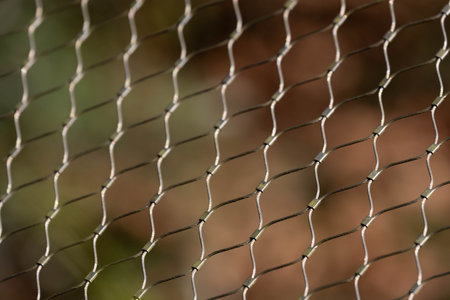 A repeating pattern of interwoven metal wires forms a delicate mesh, catching the light as it...