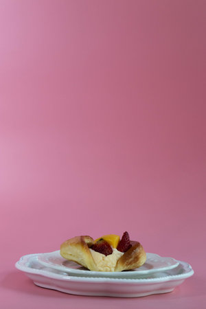 A golden, glossy Danish pastry is filled with smooth cream and topped with fresh fruit, including...