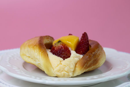 A golden, glossy Danish pastry is filled with smooth cream and topped with fresh fruit, including...