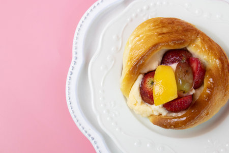 A golden, glossy Danish pastry is filled with smooth cream and topped with fresh fruit, including...