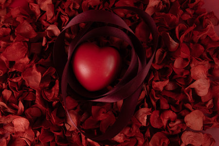 Red heart and ribbon on red rose petals background. Valentines day concept.